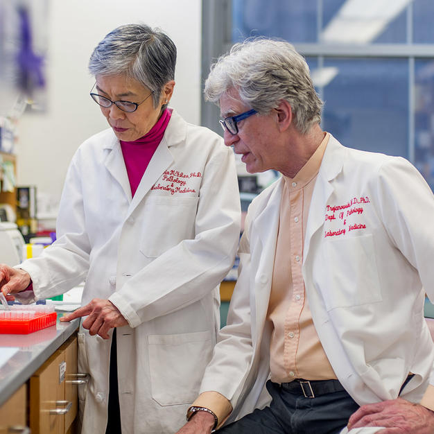 Male and female researcher wearing white lab coats chatting in the lab.