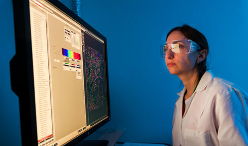 Female researcher in the lab wearing goggles while looking at a scan on the computer screen.
