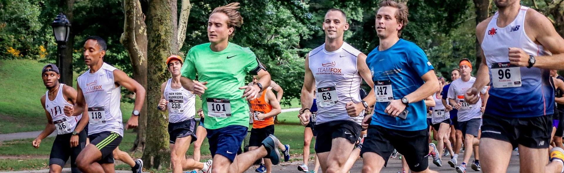 Image from a previous Run/Walk event. Half a dozen adults run in t-shirts, shorts, and marathon numbers.