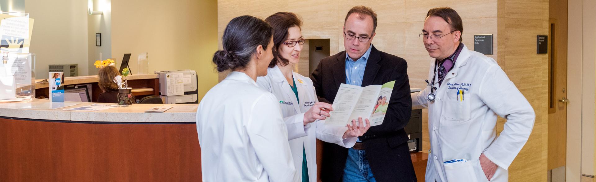 Male patient in doctor's office standing with three doctors looking at a brochure.