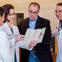 Male patient in doctor's office standing with three doctors looking at a brochure.